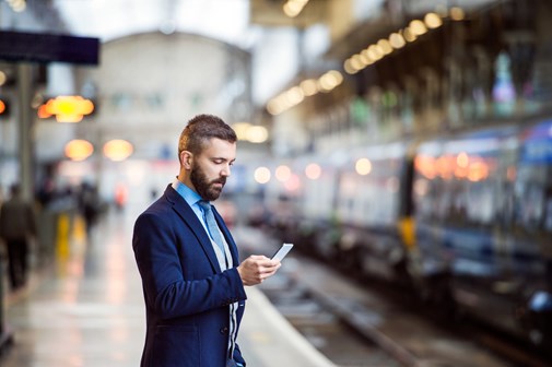 man on train platform looking at mobile